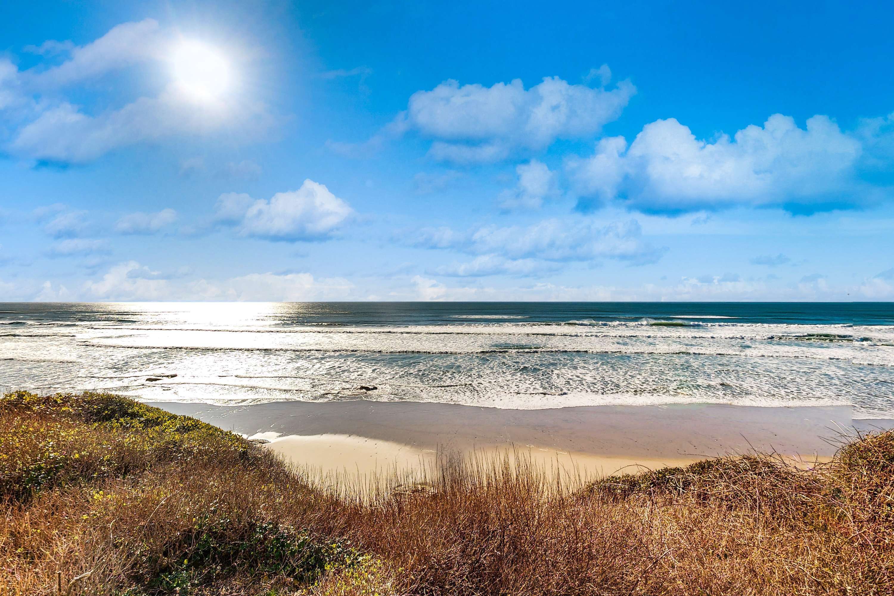 A beach with waves, a clear sky, and a sun.