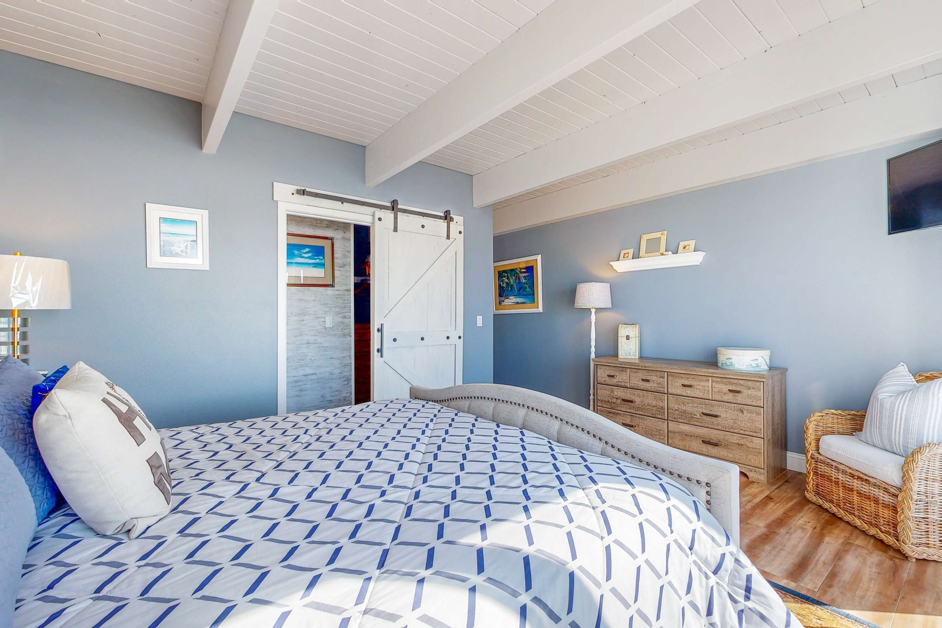 A bedroom with a bed, dresser, chair, and a door leading to another room.