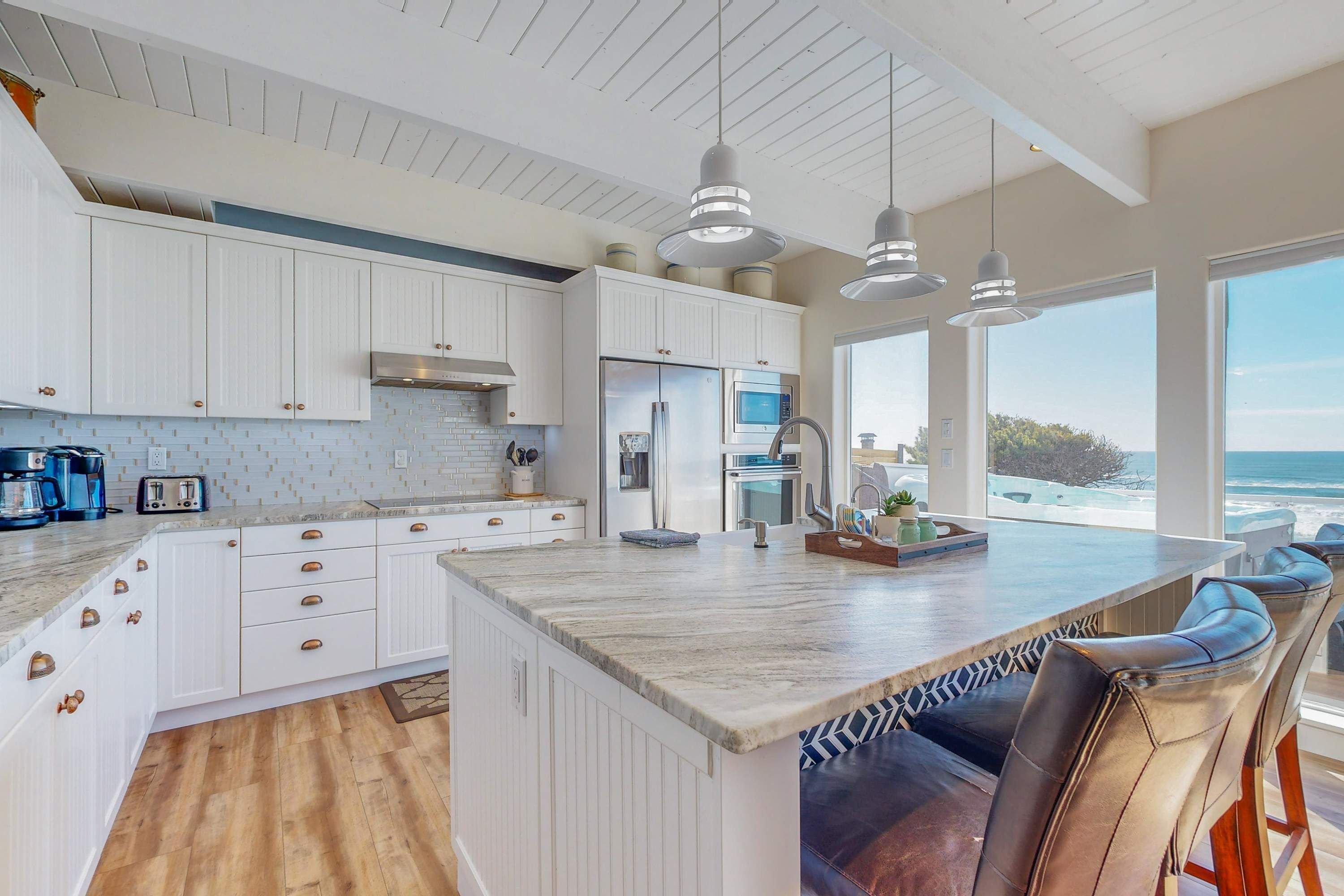 Een moderne keuken met witte kasten, een groot eiland en hanglampen.