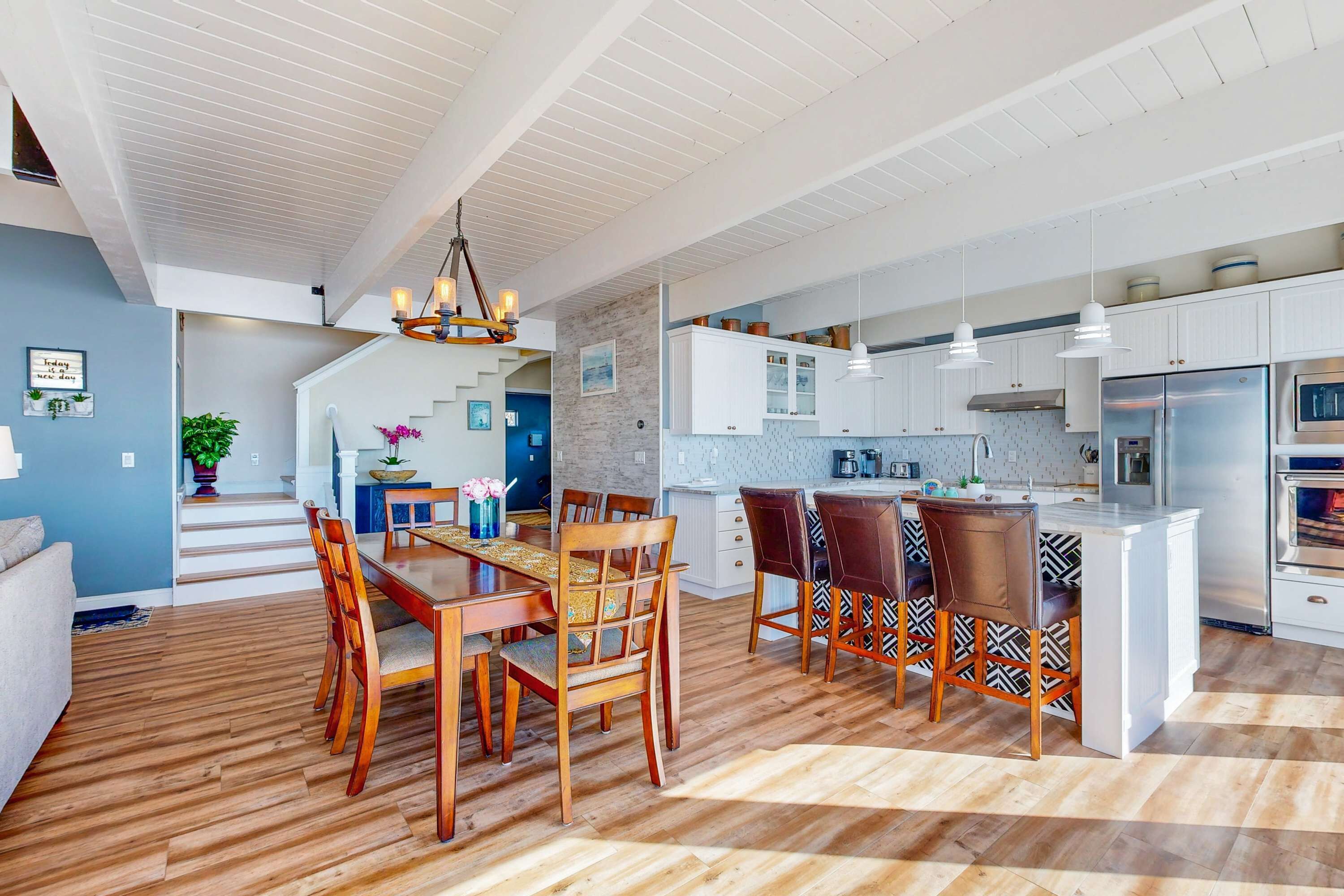 Een moderne keuken met witte kasten, een centraal eiland en een eethoek met houten stoelen.