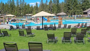 A pool area with multiple lounge chairs and umbrellas, surrounded by a grassy area and trees. - Comfortable Sunriver Home with Private Hot Tub and WiFi - Free SHARC Access (Sunriver)