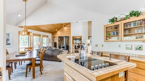 A modern kitchen with a central island, wooden cabinetry, and a dining area with a large table and chairs. - Comfortable Sunriver Home with Private Hot Tub and WiFi - Free SHARC Access (Sunriver)