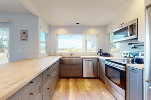 A modern kitchen with stainless steel appliances, wooden countertops, and a large window providing natural light. - Mountain escape with private hot tub, amazing views, game room & SHARC passes (Sunriver)