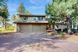 A two-story house with a garage, a covered porch, and a paved driveway. - Mountain escape with private hot tub, amazing views, game room & SHARC passes (Sunriver)