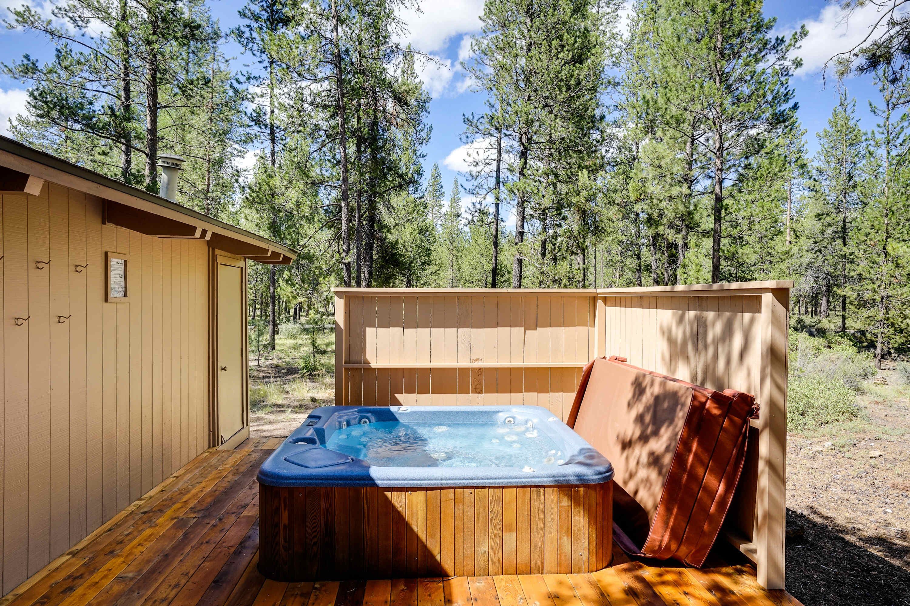 Eine Holzterrasse mit Whirlpool, ein Holzschuppen und ein bewaldeter Bereich.
