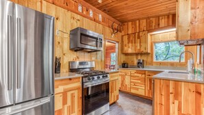 A modern kitchen with stainless steel appliances, wooden cabinetry, and a large window.