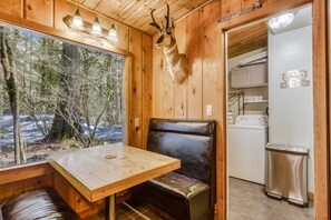 En stuga med träbord och träbänk, ett uppstoppat rådjurshuvud på väggen, en tvättmaskin och ett kylskåp.