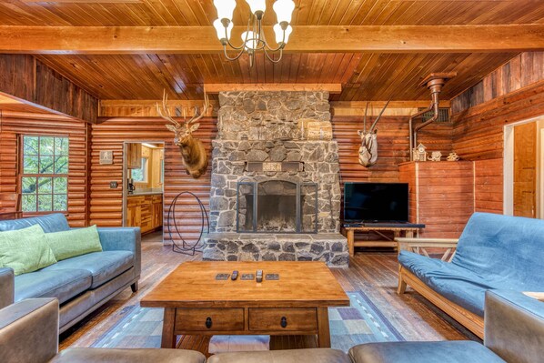 Interno di una baita di legno con camino in pietra, mobili in legno e televisore.