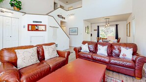 A spacious living area with two leather sofas, a coffee table, and a staircase leading to an upper level. - Charming cabin with patio, firepit, fast WiFi, full kitchen, & W&D (Manzanita)