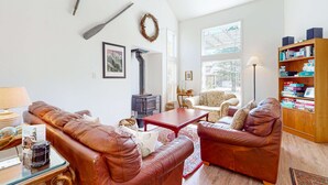 A living room with leather sofas, a fireplace, a bookshelf, and a large window. - Charming cabin with patio, firepit, fast WiFi, full kitchen, & W&D (Manzanita)