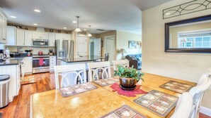 A modern kitchen with white cabinets, stainless steel appliances, and a dining area with a wooden table and chairs. - Updated home with fireplace & media room - 2 blocks to the beach & promenade (Seaside)