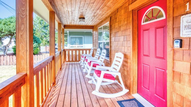 A wooden porch with rocking chairs, a red door, and a mailbox. - Updated home with fireplace & media room - 2 blocks to the beach & promenade (Seaside)
