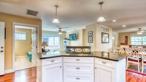 A kitchen with white cabinets, a granite countertop, pendant lighting, and a dining area with white chairs. - Updated home with fireplace & media room - 2 blocks to the beach & promenade (Seaside)