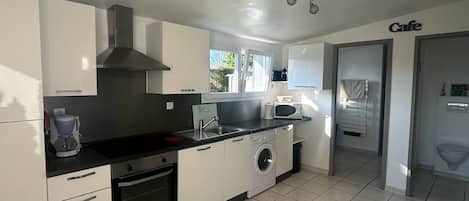 A modern kitchen with white cabinets, a black countertop, a built-in oven, a microwave, and a washing machine.
