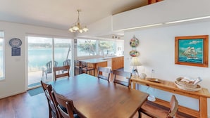 Zona pranzo con tavolo e sedie in legno, un lampadario e vista mare attraverso ampie finestre.