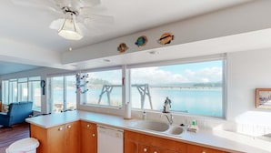 Una cucina con mobili in legno, lavastoviglie, un'ampia finestra vista mare e una ventola a soffitto.