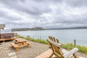 A wooden deck with picnic tables and a hot tub overlooking a river with a bridge in the distance. - Dog-Friendly Bayfront Home with Private Hot Tub, Water & Bridge Views, Free WiFi (Waldport)