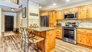A kitchen with wooden cabinets, a stainless steel refrigerator, a microwave, a stove, and a bar area with stools. - Dog-friendly home next to South Meadow pool with fireplace & washer&dryer (Black Butte Ranch)