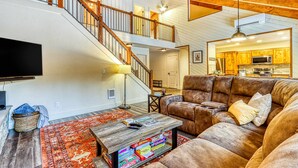 A spacious living area with a wooden staircase, a leather sofa, a coffee table, and a flat-screen TV. - Dog-friendly home next to South Meadow pool with fireplace & washer&dryer (Black Butte Ranch)
