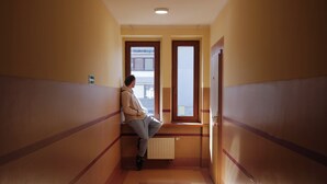 A narrow hallway with a person leaning against a wall, a radiator, and a door. - Hotel Sowa (Częstochowa)