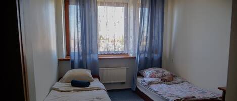 Una habitación pequeña con dos camas individuales, una ventana con cortinas, un radiador y un cabecero de madera.