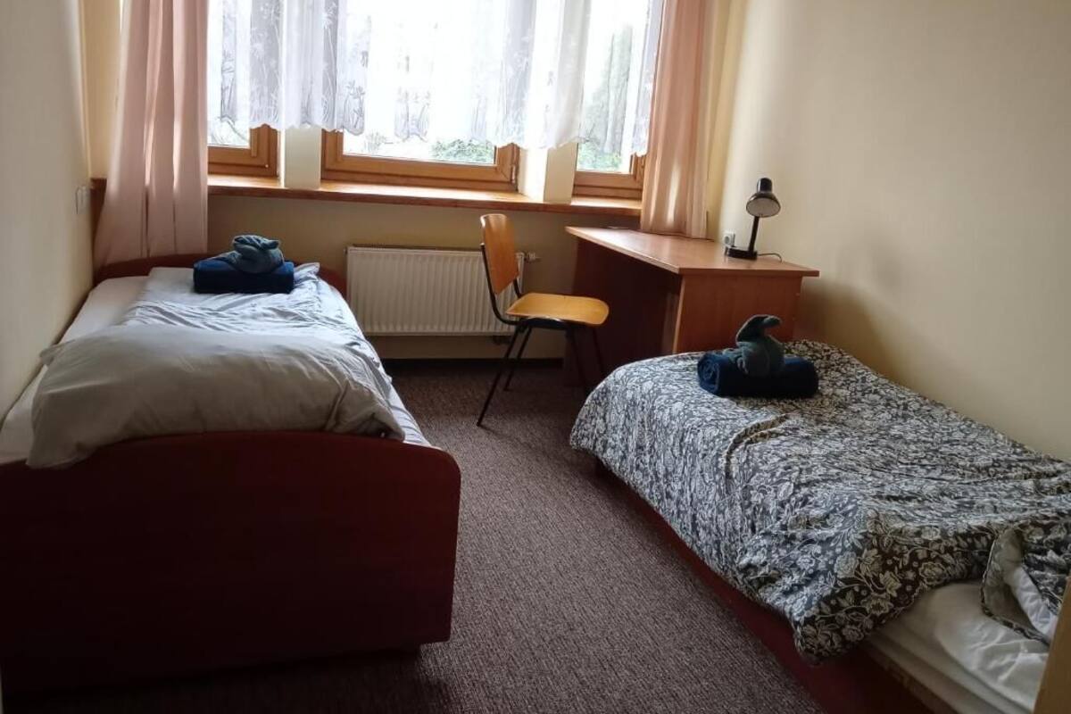 Une chambre avec deux lits, une chaise, un bureau et une fenêtre avec des rideaux.