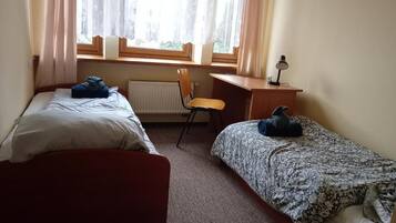 A room with two beds, a chair, a desk, and a window with curtains.