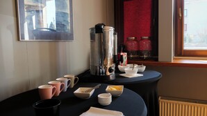 A breakfast table with coffee maker, mugs, bowls, and a window with red curtains. - Hotel Sowa (Częstochowa)