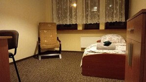 A hotel room with a single bed, a chair, a radiator, and a window with a curtain. - Hotel Sowa (Częstochowa)