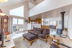 A spacious living area with a sofa, ottoman, and a television. - Exquisite home with spectacular views, deck, gas fireplace & game room (Gold Beach)