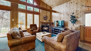 A wooden interior with a fireplace, sofas, a television, and a stone fireplace surround. - Log decor home with private hot tub, deck & shared pools & tennis (Eagle Crest)
