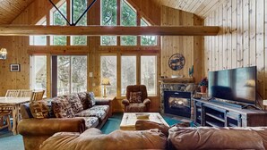 A cozy cabin interior with a large sofa, a fireplace, a television, and a dining area. - Log decor home with private hot tub, deck & shared pools & tennis (Eagle Crest)