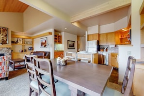 Una cocina moderna con armarios de madera, un comedor con una mesa grande y sillas, y una sala de estar acogedora con chimenea.