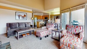 A living room with a sofa, armchairs, a coffee table, and a dining area with a kitchen in the background. - Charming waterfront condo with pool, tennis, hot tub, balcony, & W&D (Eagle Crest)