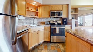 A modern kitchen with stainless steel appliances, wooden cabinets, and a stone tile backsplash. - Charming waterfront condo with pool, tennis, hot tub, balcony, & W&D (Eagle Crest)