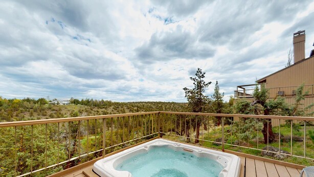A hot tub on a wooden deck with a view of a forested landscape. - Charming waterfront condo with pool, tennis, hot tub, balcony, & W&D (Eagle Crest)
