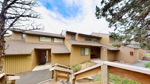 A multi-story building with a wooden deck and stairs leading to the entrance. - Charming waterfront condo with pool, tennis, hot tub, balcony, & W&D (Eagle Crest)