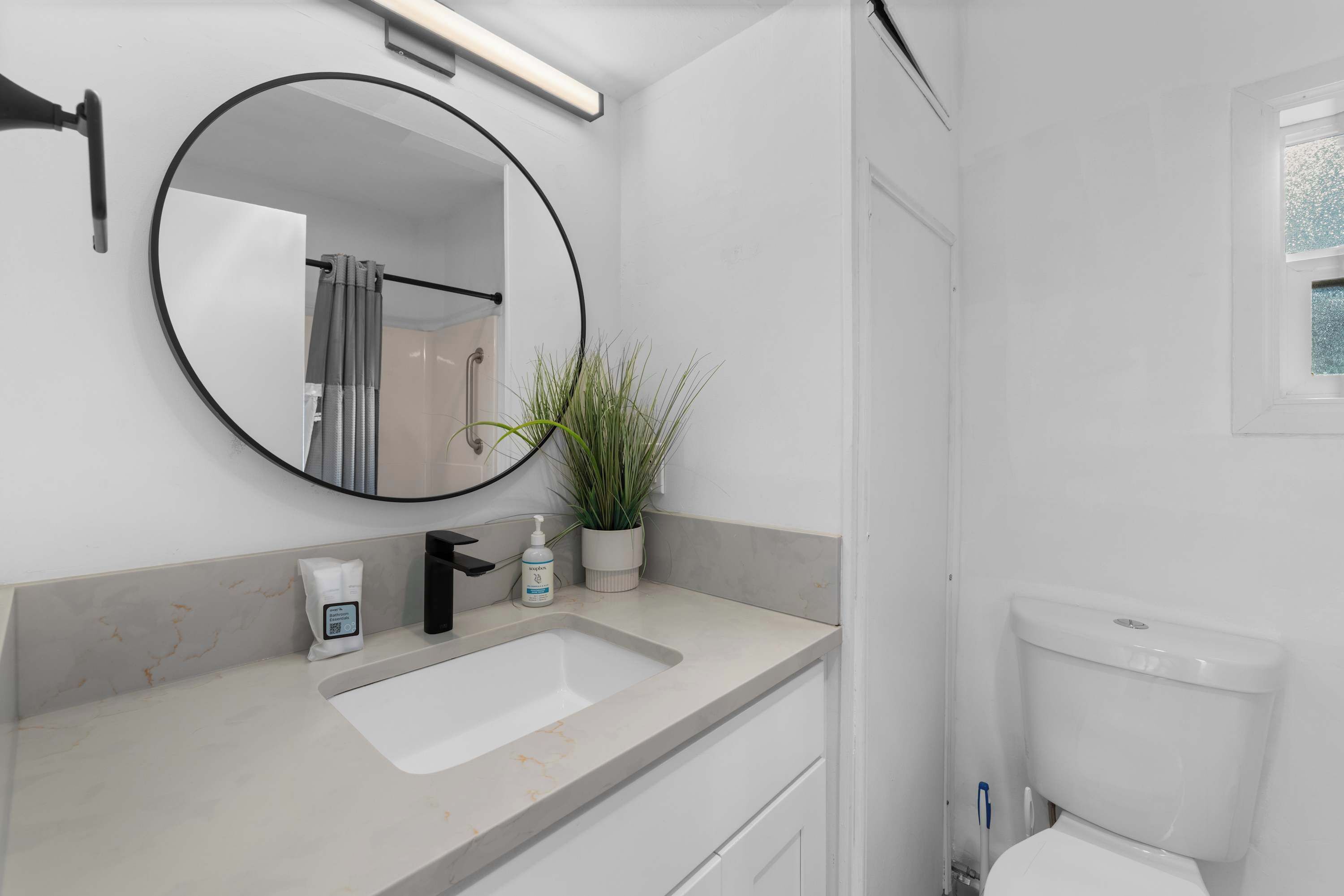 Une salle de bain avec un miroir rond, un lavabo, des toilettes et une plante en pot.