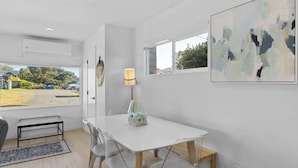 A modern dining area with a white table, clear chairs, a lamp, and a painting on the wall. - Cozy Seaside Bungalow, Brand New Hot Tub, Fast WiFi & W&D - Walk to the Beach (Seaside)