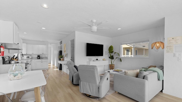 A modern kitchen with white cabinets, a dining table, and a TV mounted on the wall. - Cozy Seaside Bungalow, Brand New Hot Tub, Fast WiFi & W&D - Walk to the Beach (Seaside)