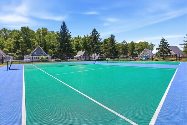 Un court de tennis avec un filet, entouré de maisons et d’arbres.