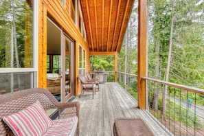 A wooden deck with wicker furniture, a grill, and a view of the forest.