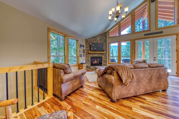 A spacious living room with a fireplace, large windows, and a wooden staircase.
