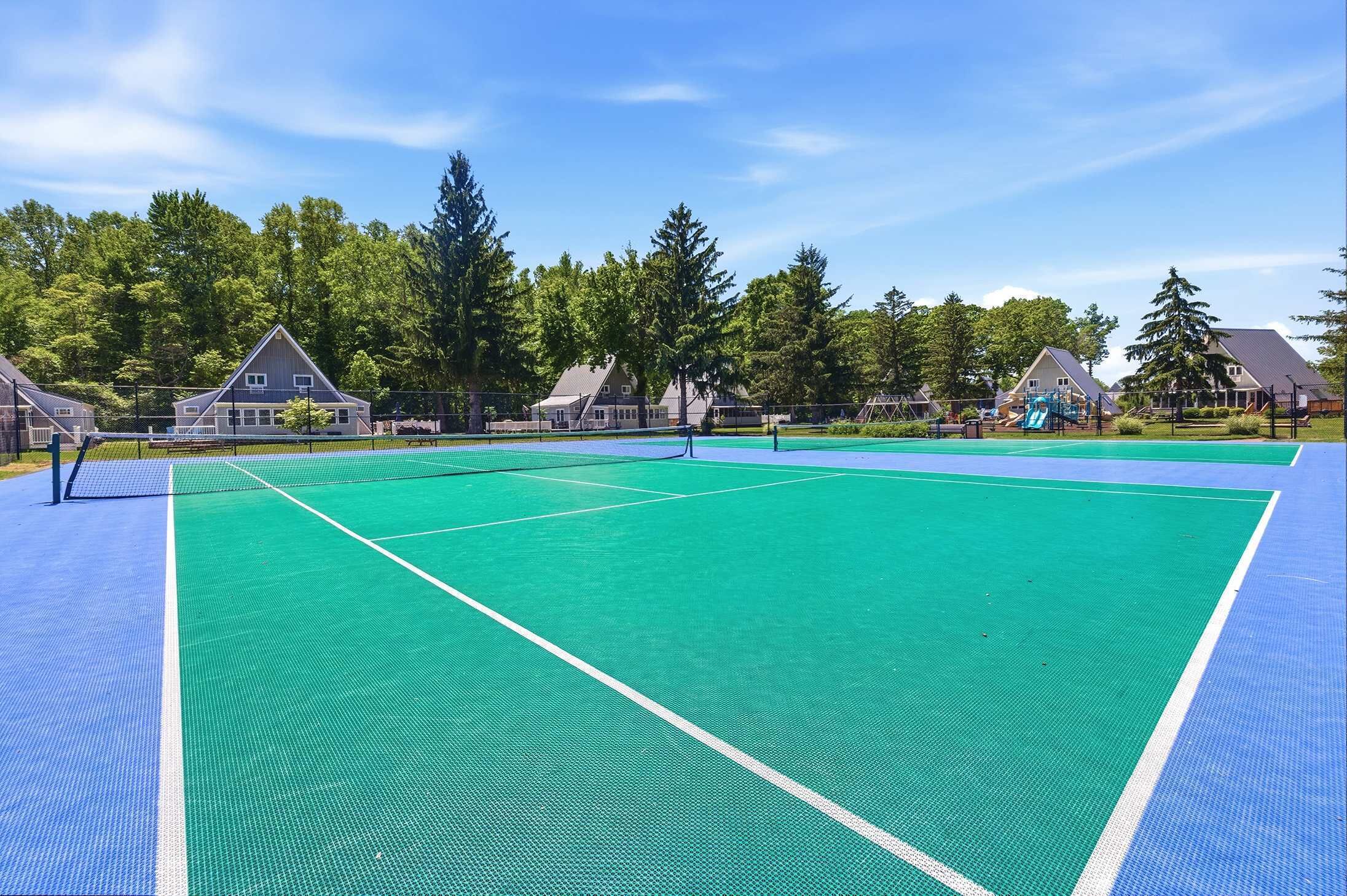 A tennis court with a net, surrounded by houses and trees.