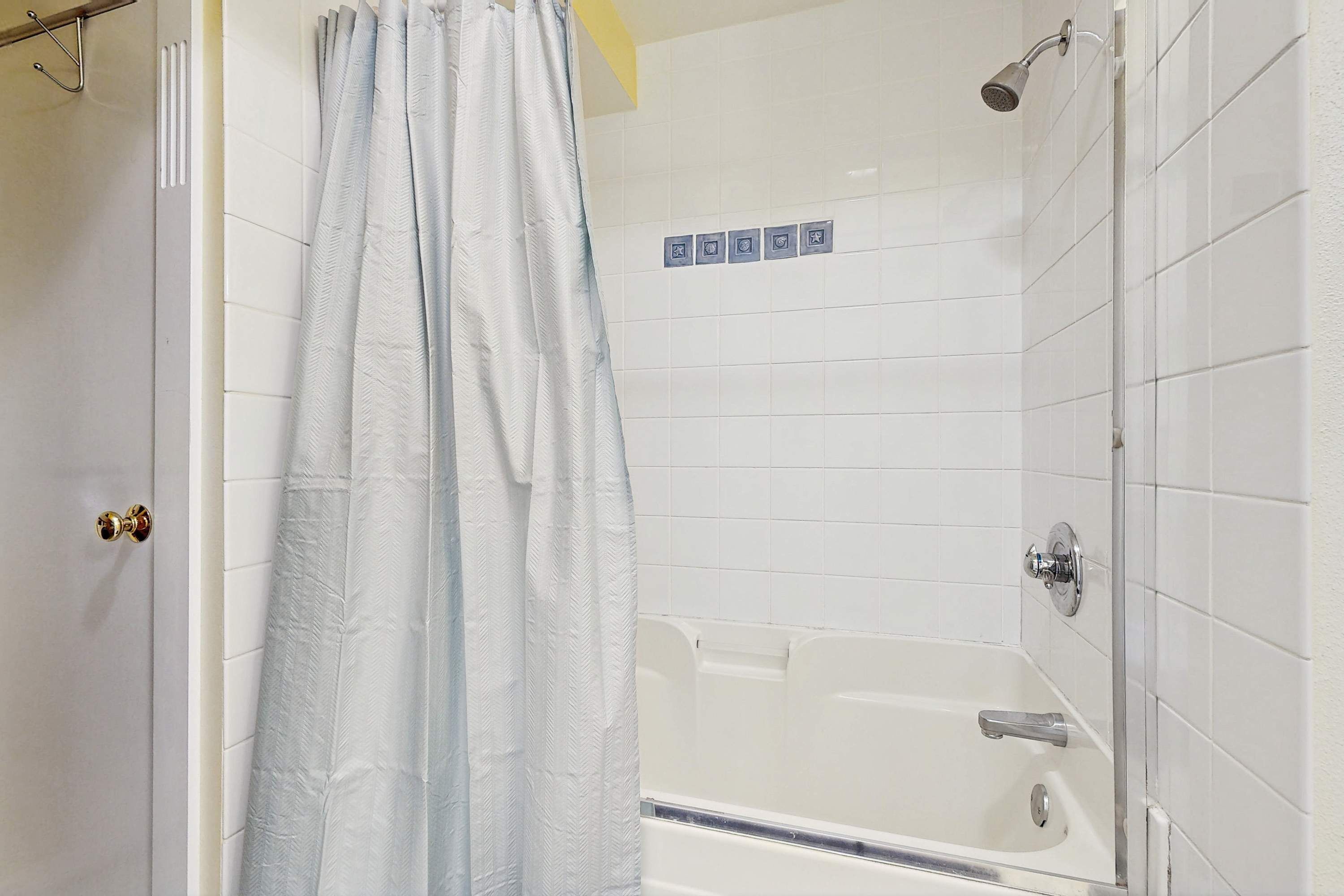 A bathroom with a bathtub, shower, and a door with a handle.