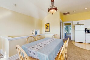 A dining room with a table, chairs, a chandelier, and a kitchen area with appliances. - Ocean-view home with private hot tub, fireplace & grill - walk to beach (Newport)