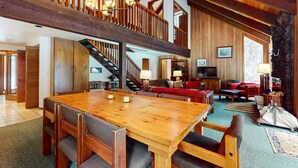A spacious living area with a wooden dining table, comfortable seating, a staircase, and a television. - Beautiful and spacious family-friendly home with indoor hot tub, fireplace, patio (Black Butte Ranch)