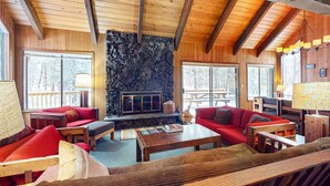 A cozy interior with wooden beams, a stone fireplace, and seating areas. - Beautiful and spacious family-friendly home with indoor hot tub, fireplace, patio (Black Butte Ranch)