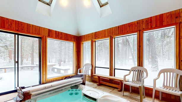 A wooden-paneled room with a hot tub, large windows, and a view of a snowy forest. - Beautiful and spacious family-friendly home with indoor hot tub, fireplace, patio (Black Butte Ranch)