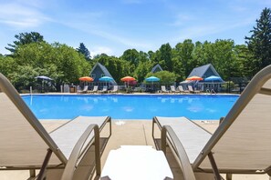 Ein Schwimmbad mit Liegestühlen und Sonnenschirmen, umgeben von Bäumen und Gebäuden.